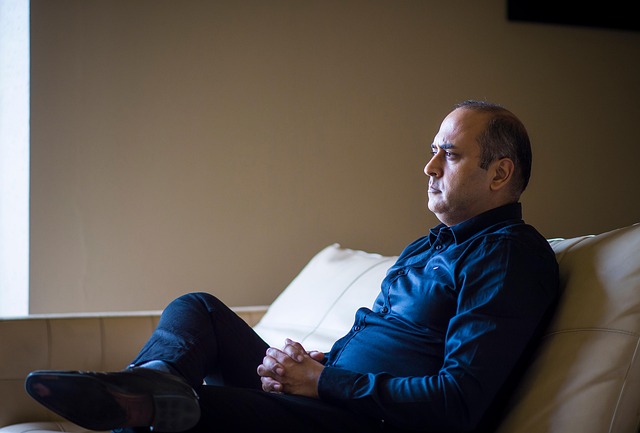 A middle-aged man sitting pensively on a couch