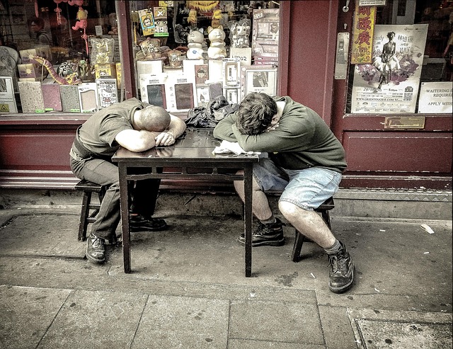 Two men resting their heads on a table outside a store