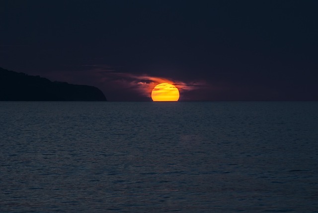 A bright sun setting or rising over the dark ocean horizon