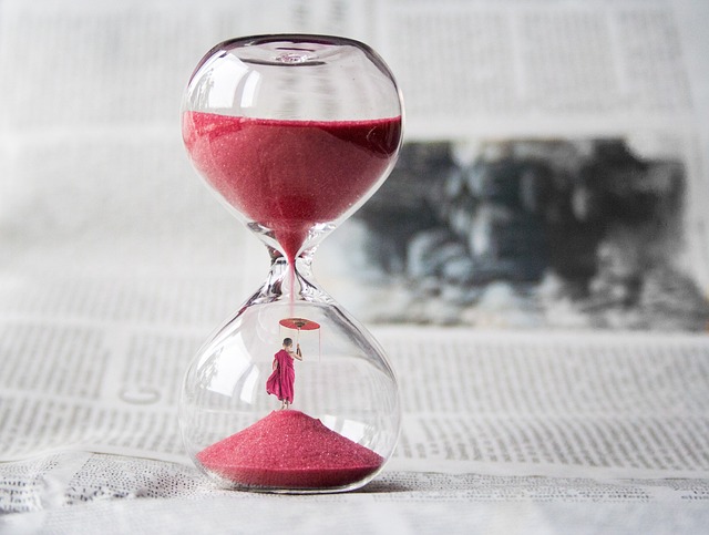 An hourglass with red sand and a tiny figure with umbrella