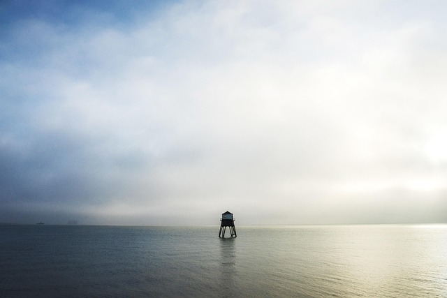 A small structure in calm water under a hazy dawn sky