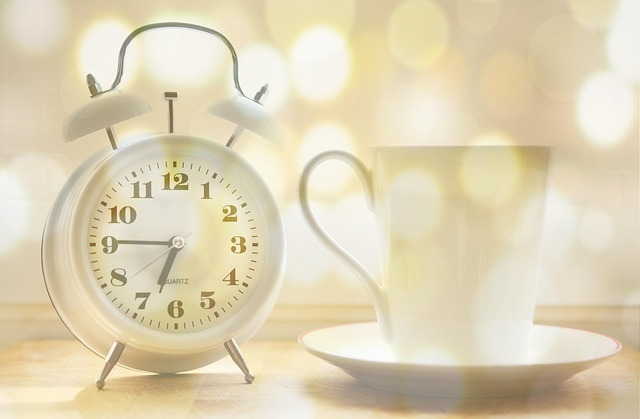 A white analog alarm clock sitting next to a mug