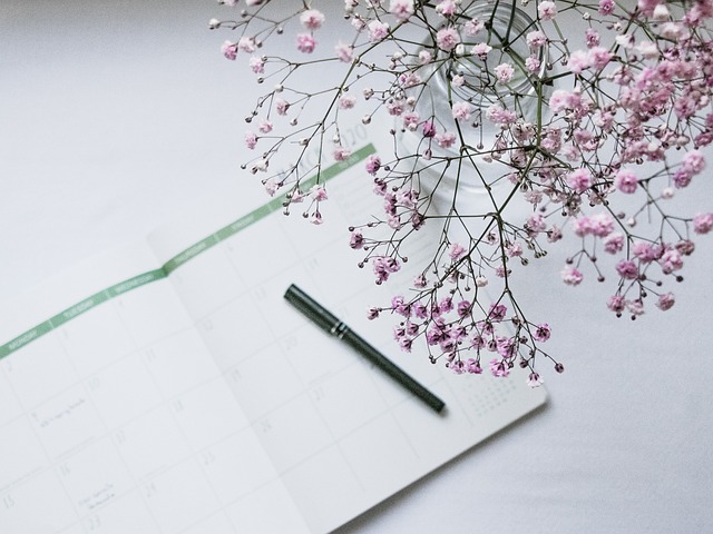 An open calendar planner with a pen and pink flowers