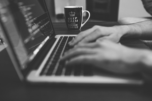 Hands typing on a laptop keyboard near a coffee mug